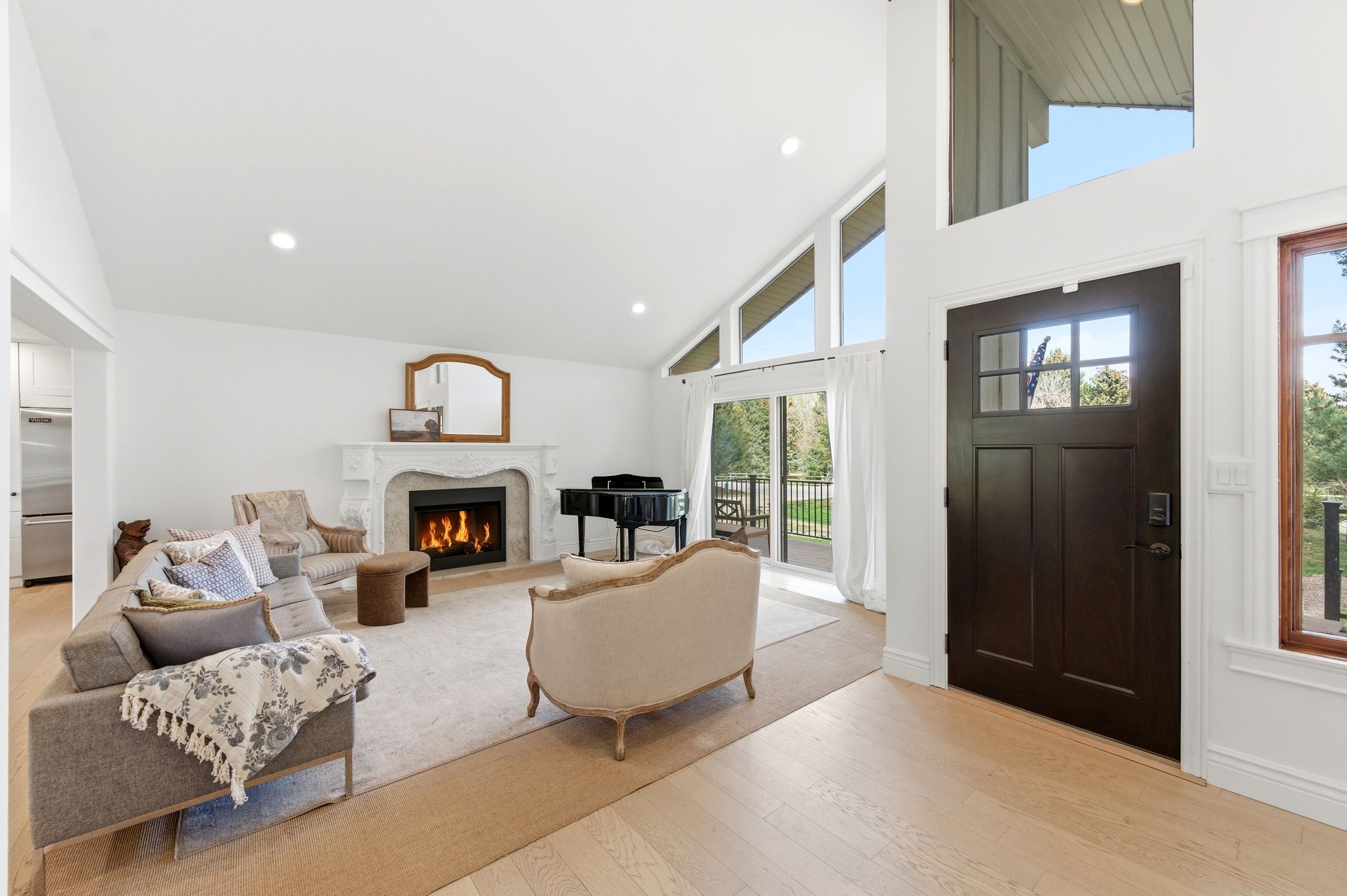 Vaulted living room with ornate fireplace, grand piano, and front entry