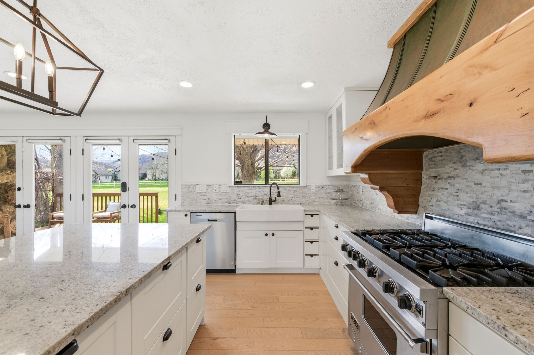Updated kitchen with granite island, wood range hood, and French doors to the deck